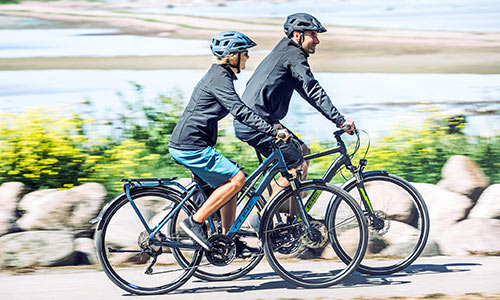 Un hombre y una mujer van en bicicletas de trekking junto al mar.