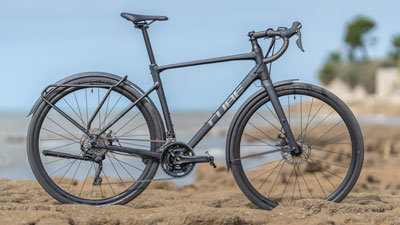 Se ve una bicicleta Cube gravel negra, situada en un paisaje rocoso, con la costa al fondo.