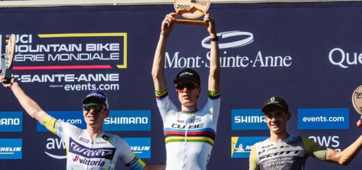 Finn Treudler celebra en la final de temporada del Cube Factory Racing 2025 en Mont-Sainte-Anne, sosteniendo el trofeo en sus manos, flanqueado por los ciclistas que ocuparon el segundo y tercer lugar en el podio.