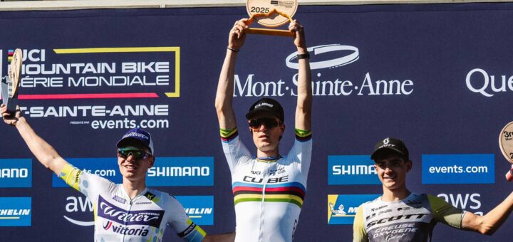 Finn Treudler celebra en la final de temporada del Cube Factory Racing 2025 en Mont-Sainte-Anne, sosteniendo el trofeo en sus manos, flanqueado por los ciclistas que ocuparon el segundo y tercer lugar en el podio.