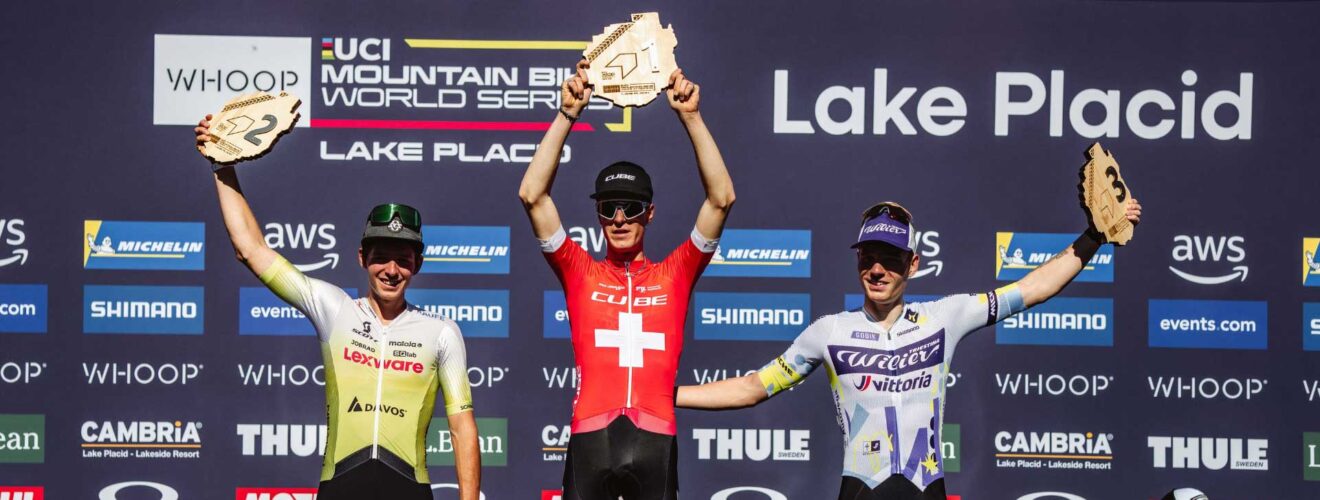 Finn Treudler celebra en el podio, levantando con orgullo el trofeo por su triunfo sub-23 en Lake Placid.
