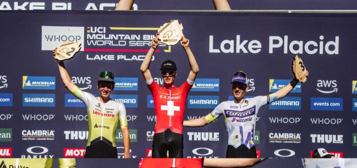 Finn Treudler celebra en el podio, levantando con orgullo el trofeo por su triunfo sub-23 en Lake Placid.